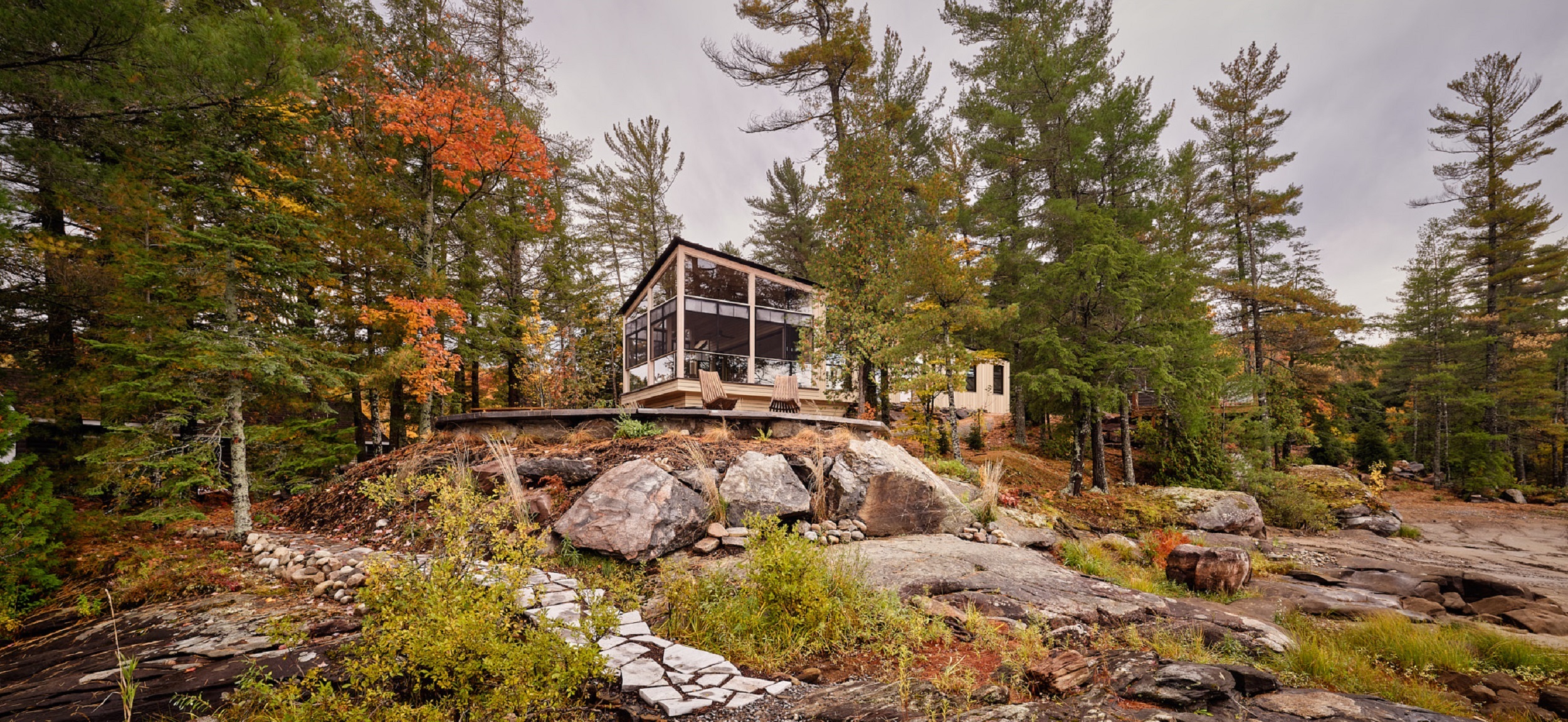 A timber and glass cottage set among the rocks and trees of the Algonquin Highlands.