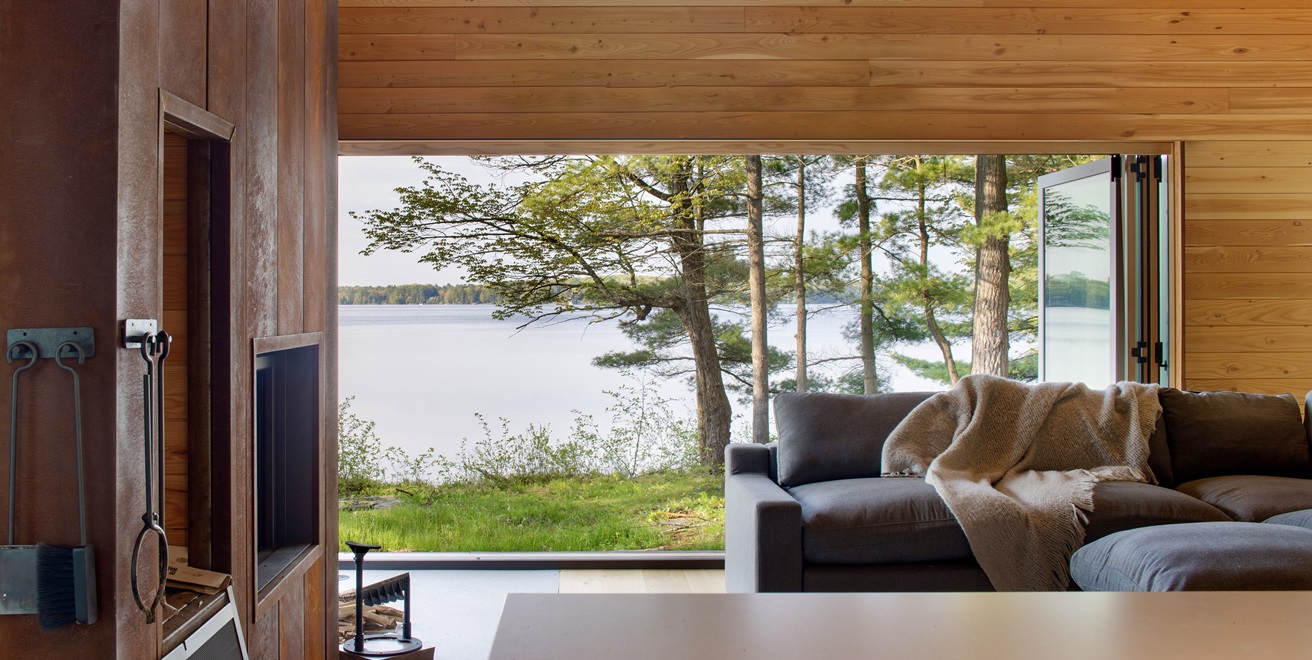 Open cottage doors connect a sitting room with trees and the lake.